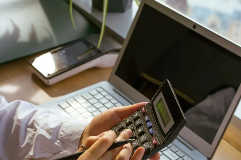 Iemand maakt berekeningen met een rekenmachine en laptop — afwegen tussen sparen en beleggen