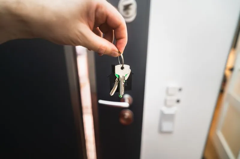 Hand houdt huissleutels omhoog aan een sleutelhanger in de vorm van een huisje
