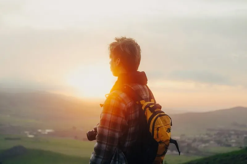Wandelaar met rugzak kijkt bij zonsopkomst uit over het landschap